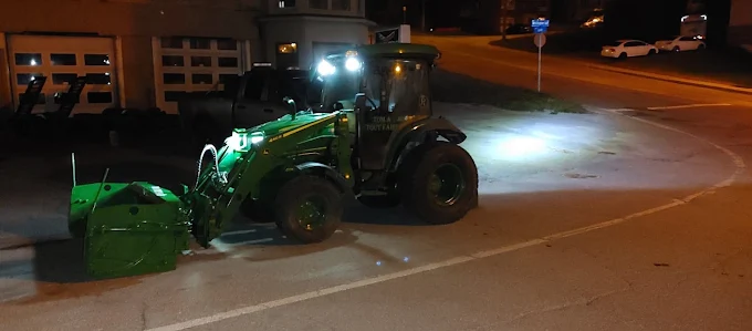Déneigement de nuit au tracteur devant un immeuble